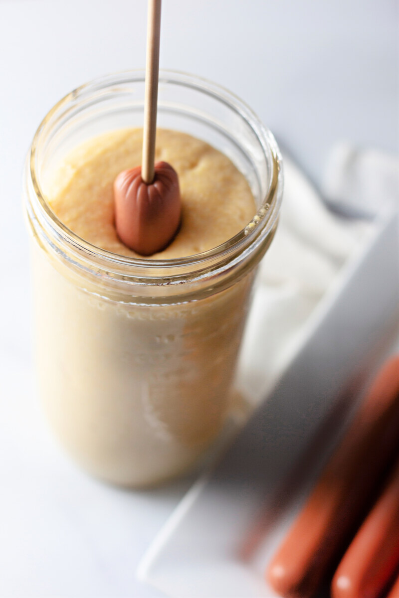 Coating a corn dog in batter in a tall glass