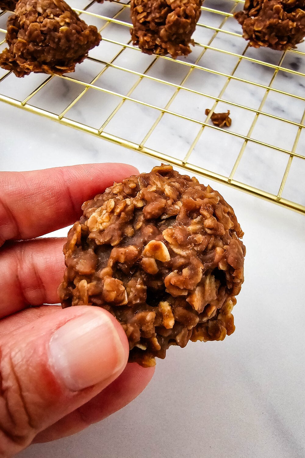 A hand holding a no-bake cookie up close, showing the chewy oat and chocolate texture.