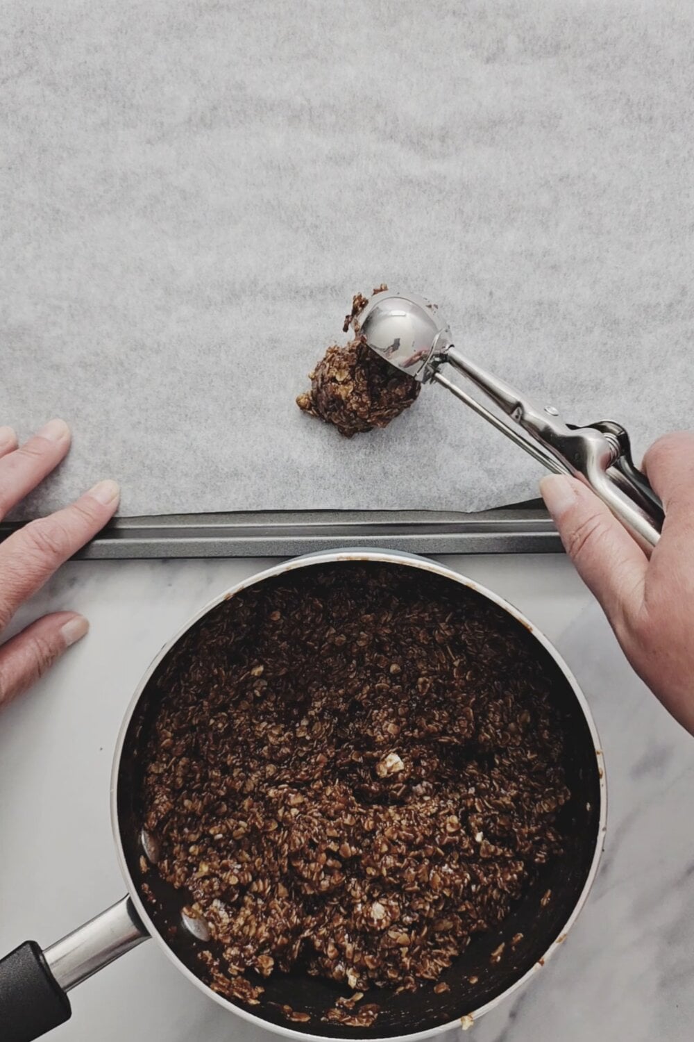 A cookie scoop dropping no-bake cookie dough onto a parchment-lined baking sheet.