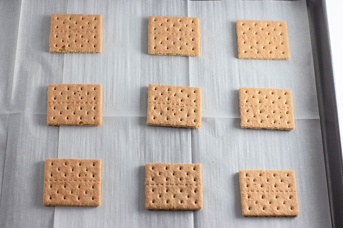 Graham cracker squares lined up on a parchment-lined baking sheet