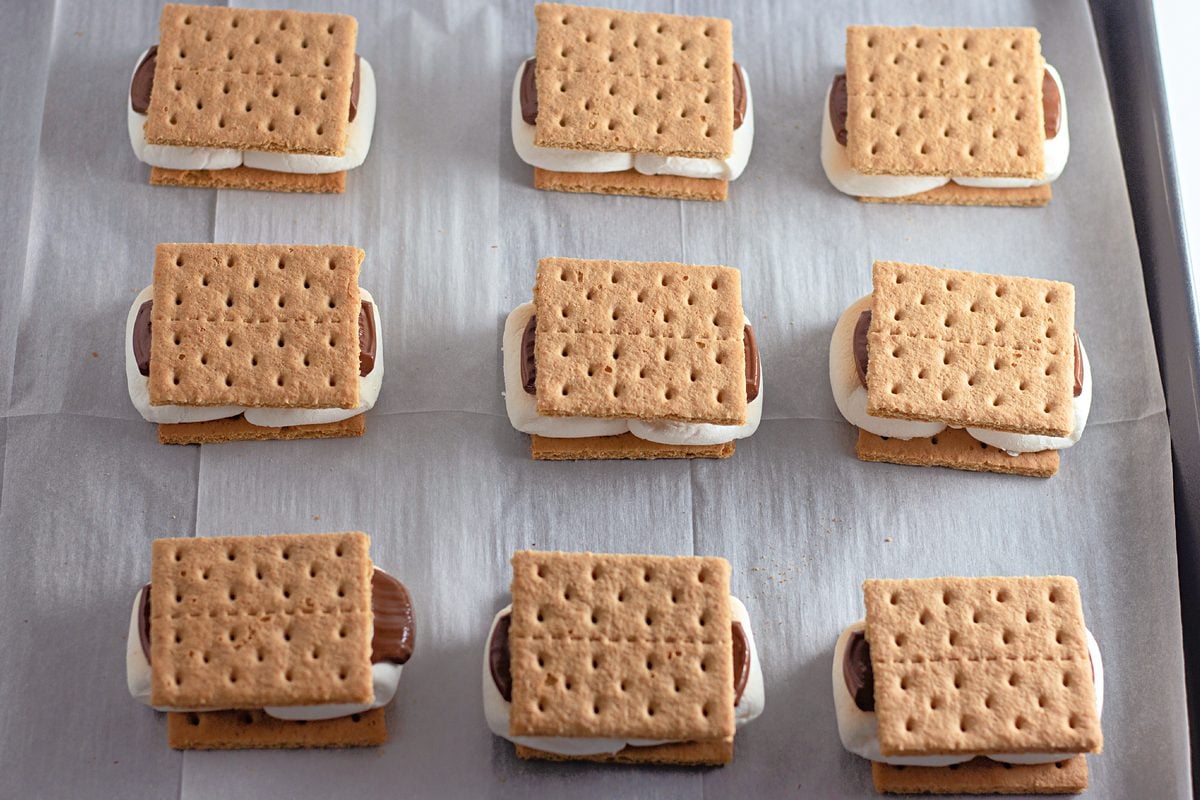 Assembled oven baked s'mores on a parchment-lined sheet