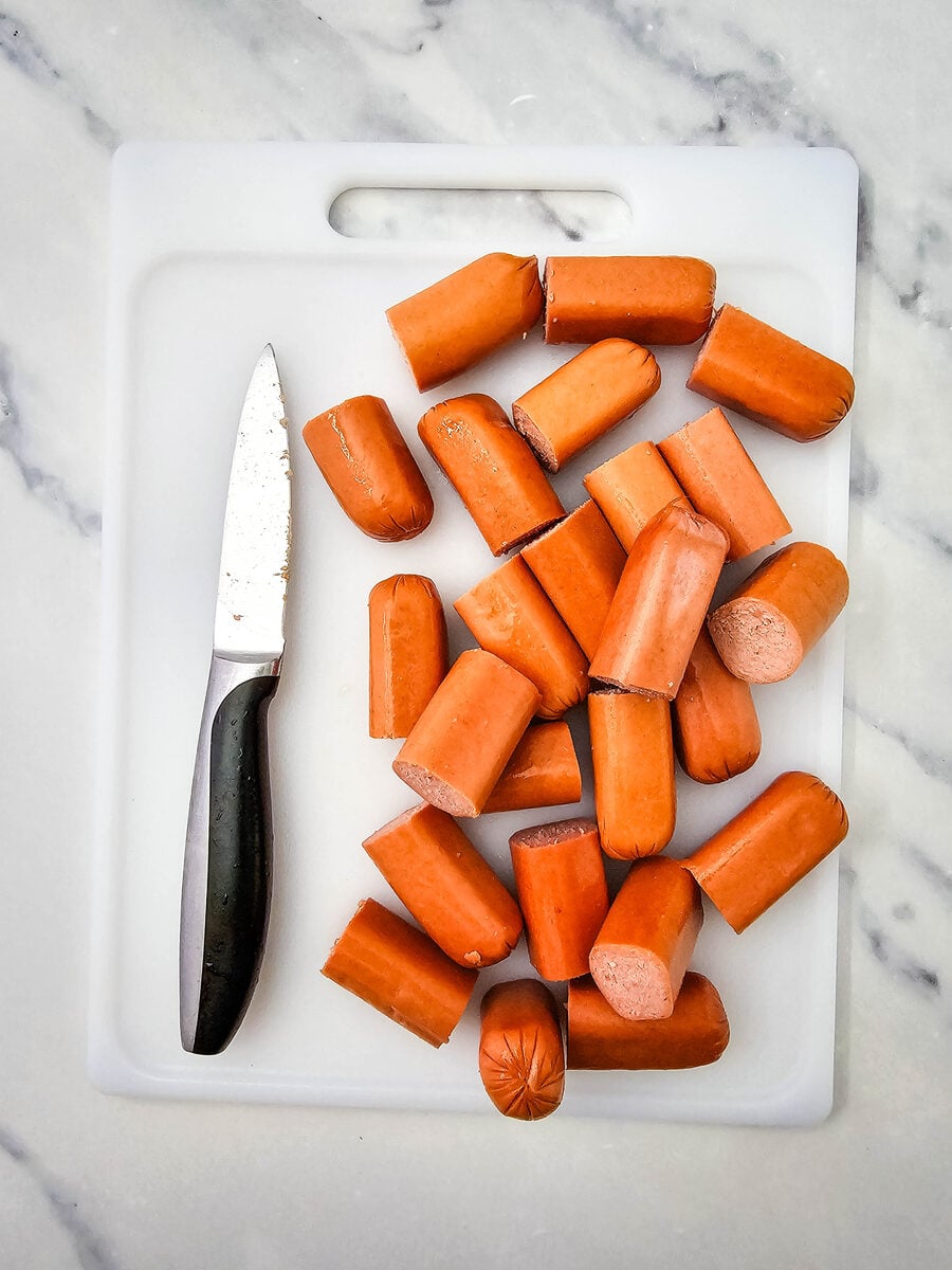 Beef hot dogs cut into thirds on a cutting board