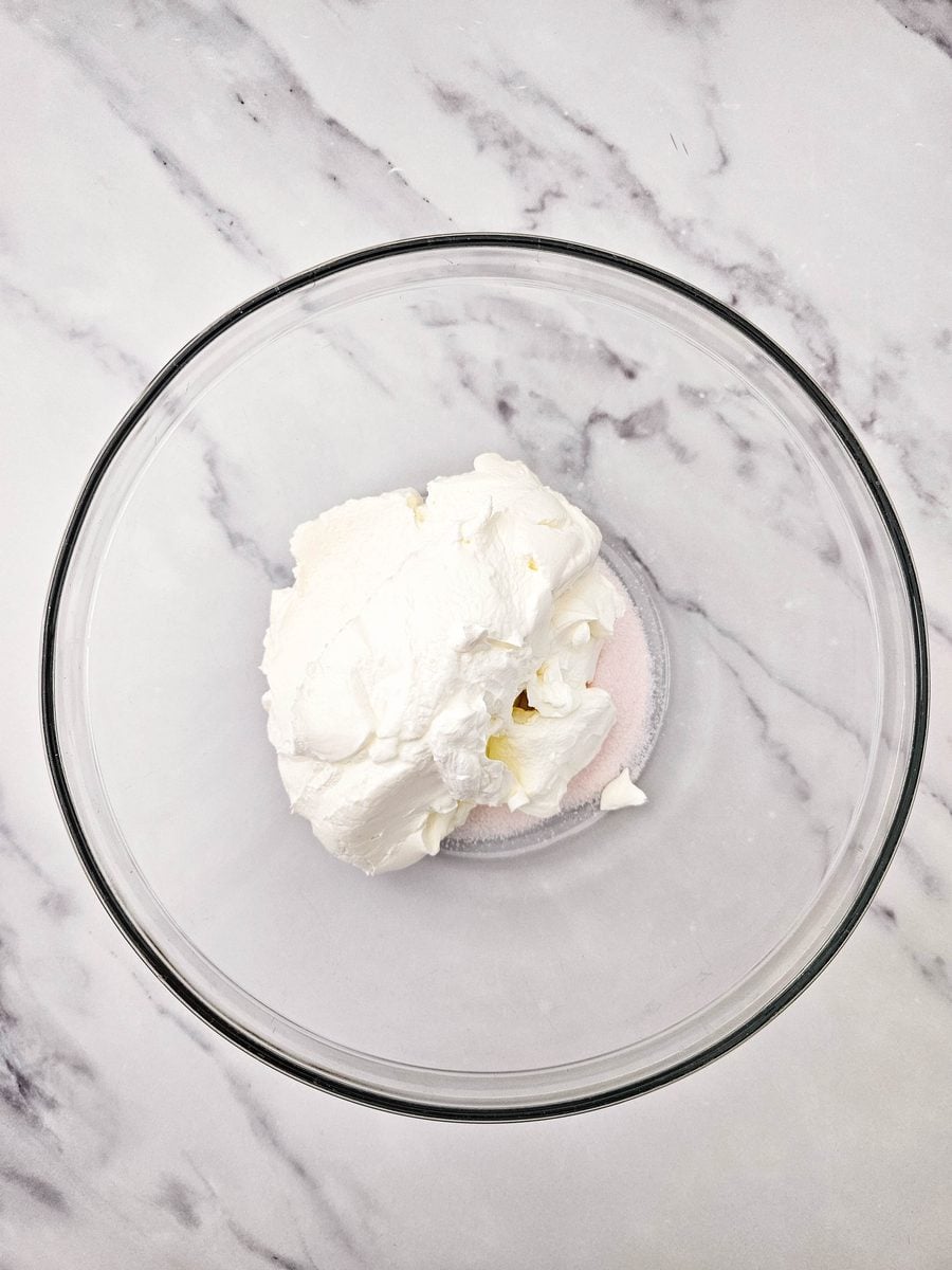 Sour cream added to orange gelatin powder in a bowl