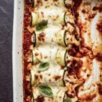 Zucchini rollatini baked in a white dish topped with marinara, melted mozzarella, and fresh basil