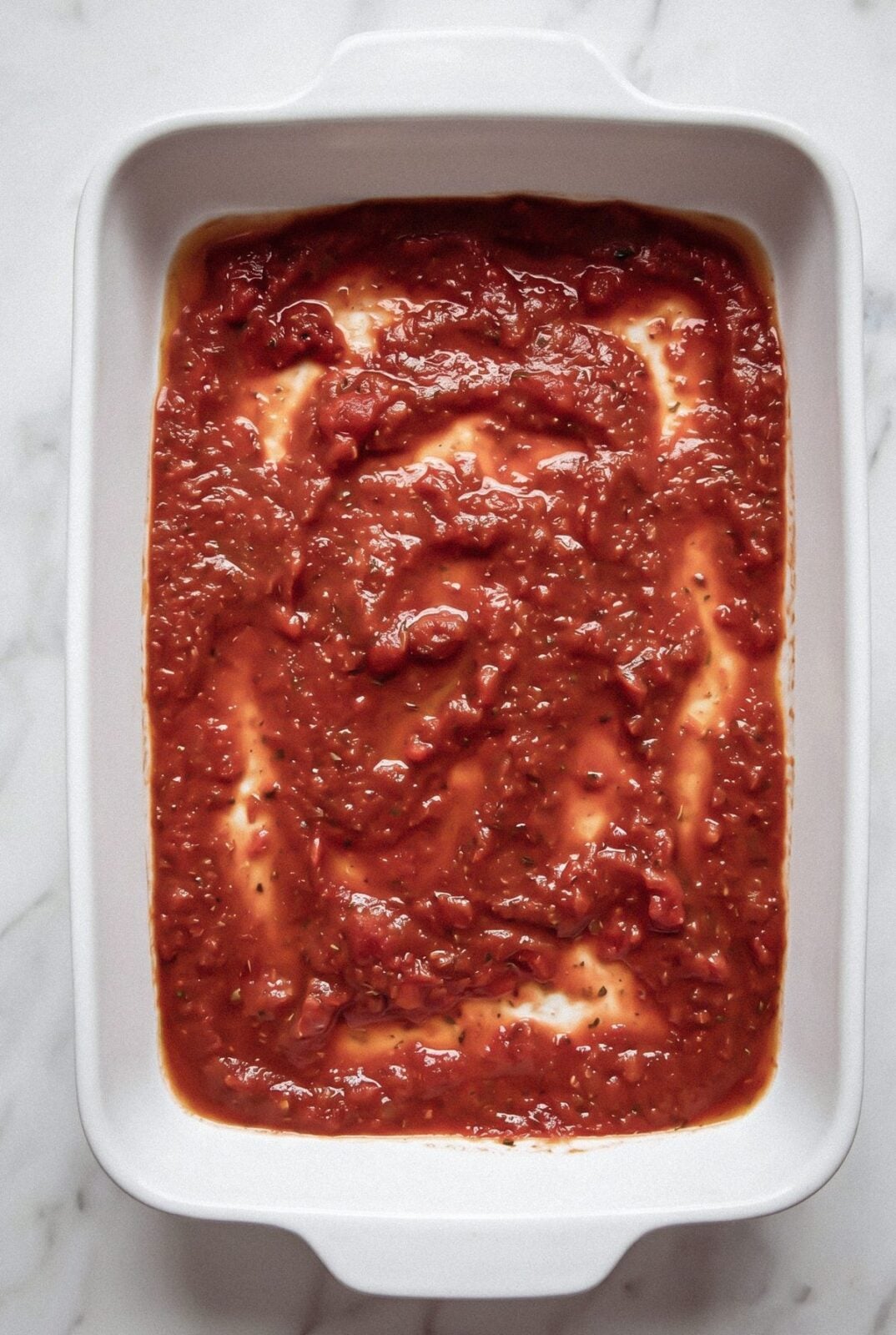 Marinara sauce spread in the bottom of a baking dish