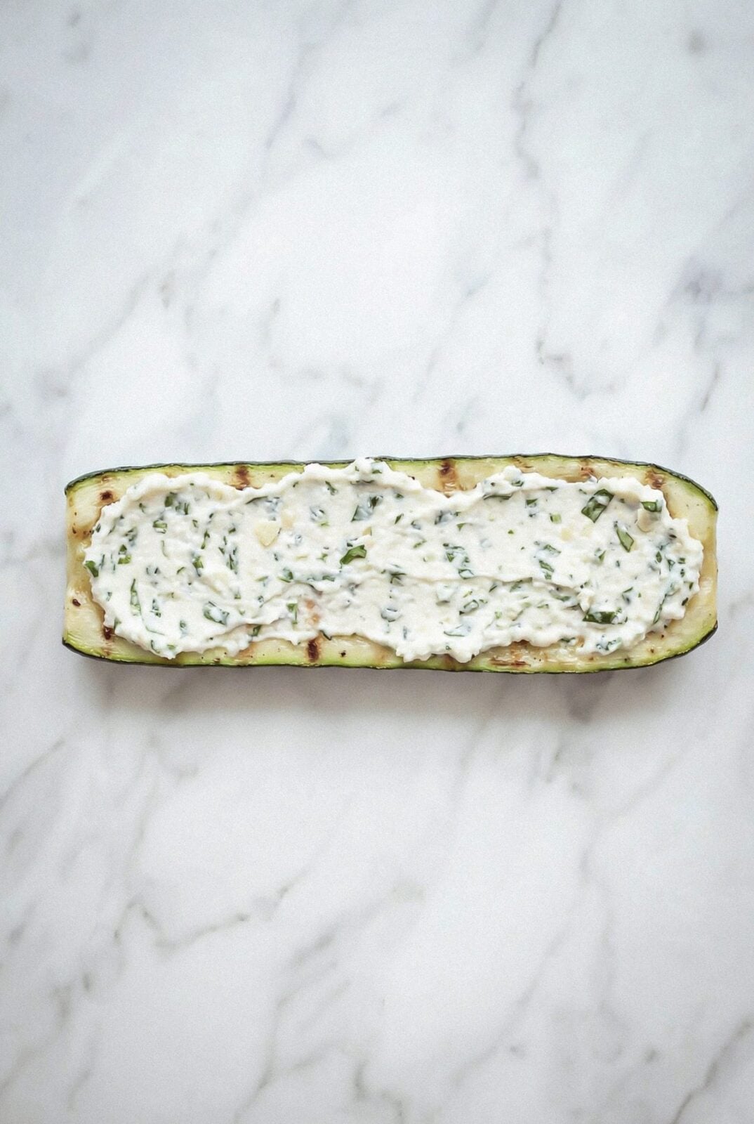 A grilled zucchini strip spread with ricotta filling ready to roll