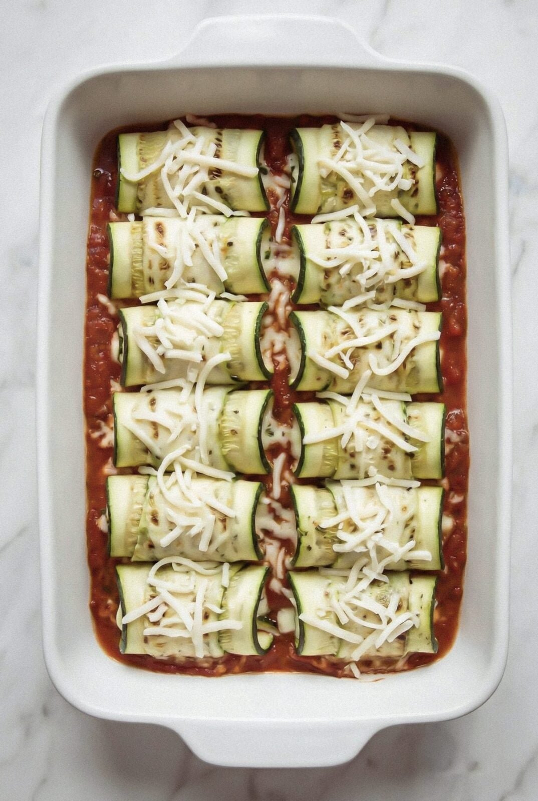 Zucchini rollatini topped with shredded mozzarella before baking