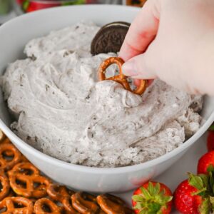 Hand dipping into a white bowl of OREO dip with a small pretzel
