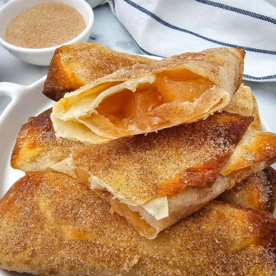 A stack of crispy apple pie filling egg rolls with cinnamon sugar coating