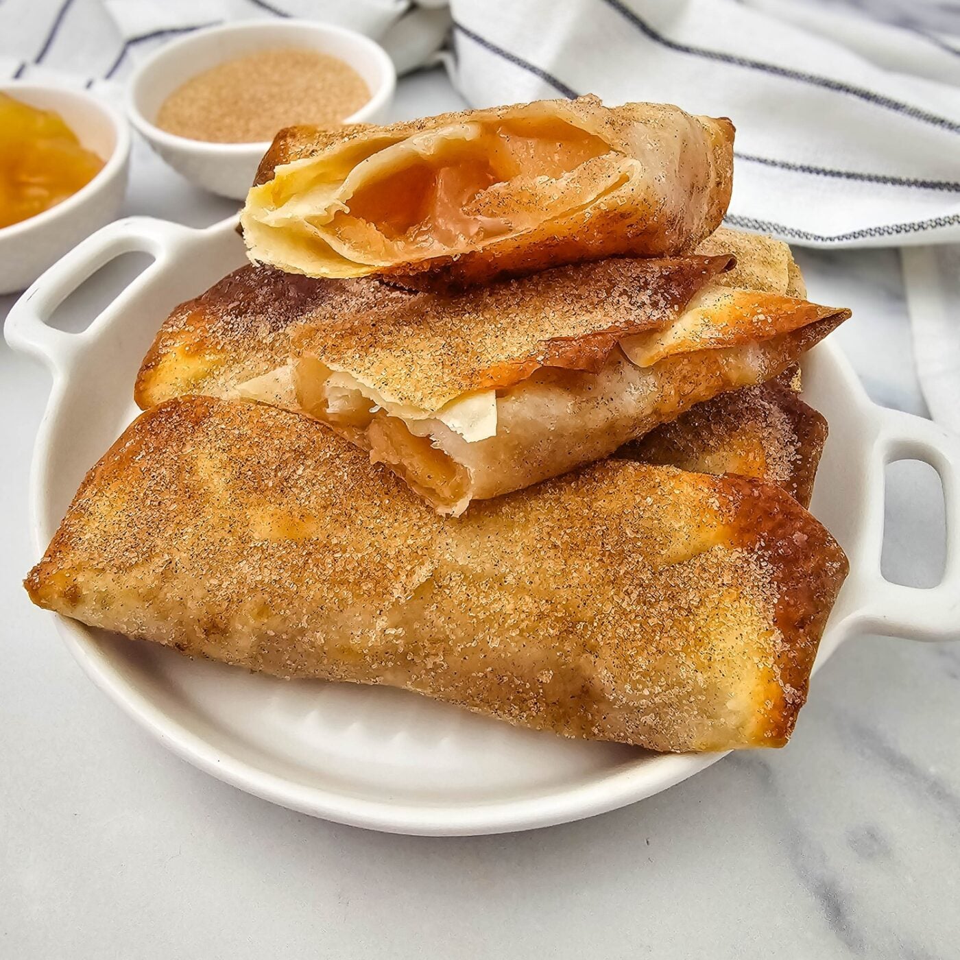 Air fryer apple pie filling egg rolls cut open to show warm apple filling, coated in cinnamon sugar