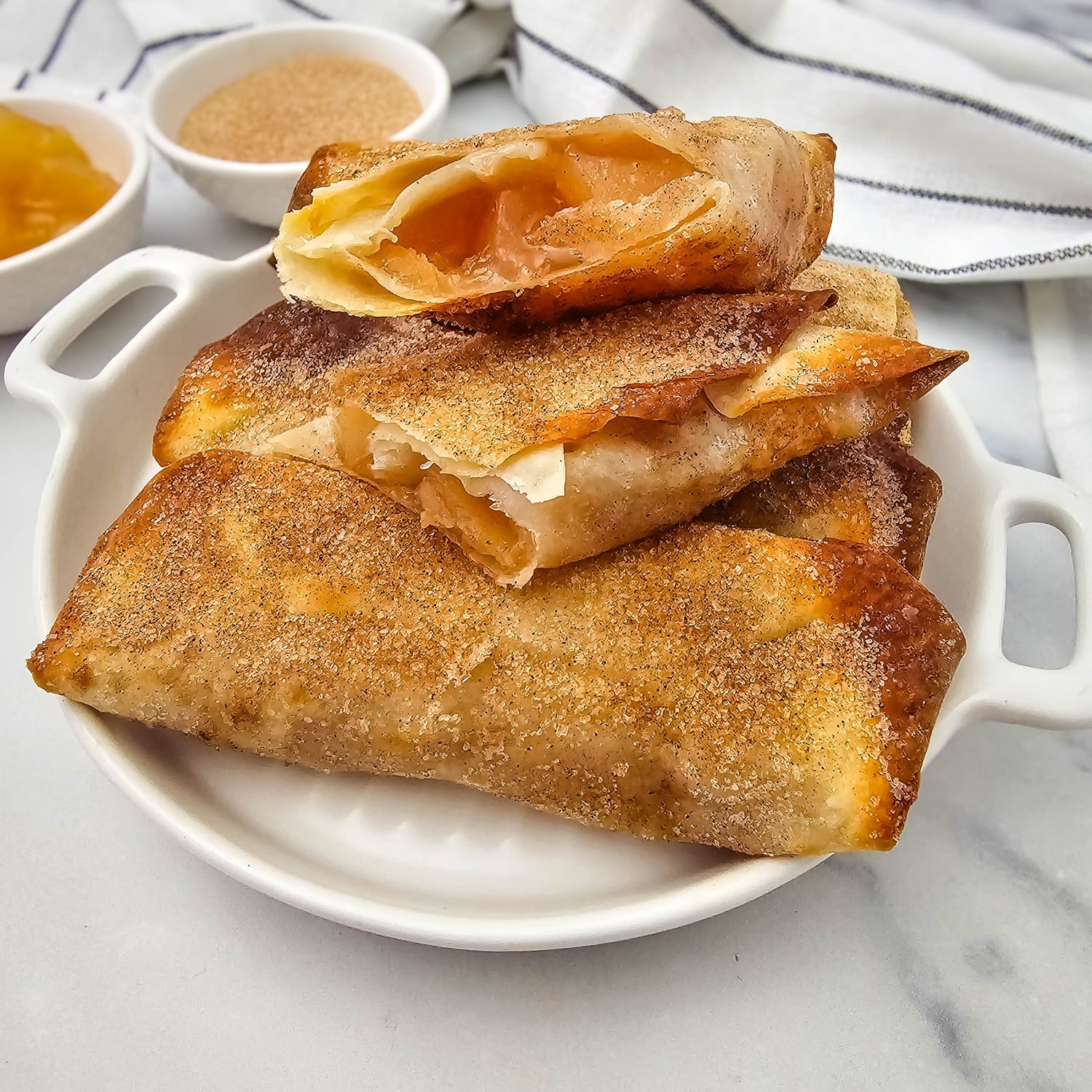 Air fryer apple pie filling egg rolls cut open to show warm apple filling, coated in cinnamon sugar