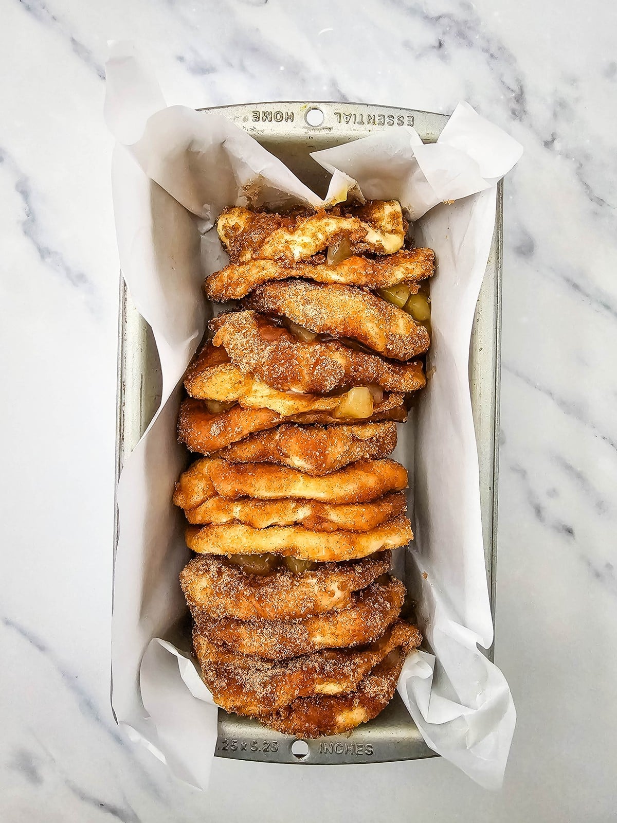 Biscuit stacks arranged sideways in a parchment lined loaf pan before baking