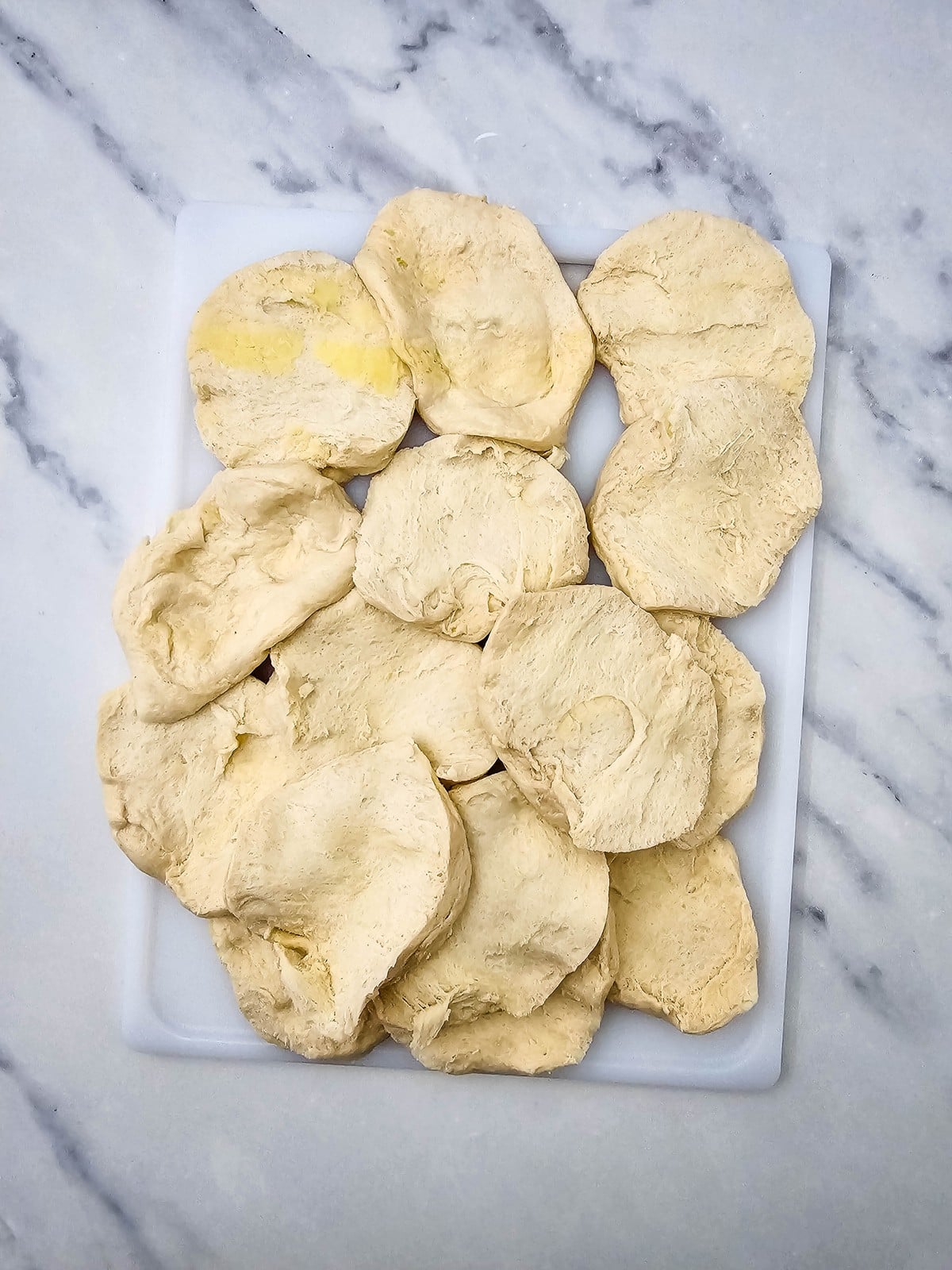 Canned flaky biscuits pulled apart into thin rounds on a cutting board