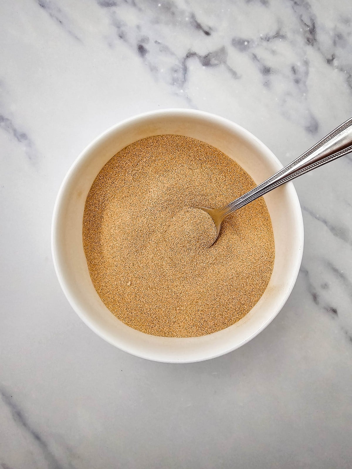 Cinnamon sugar mixed in a white bowl with a spoon