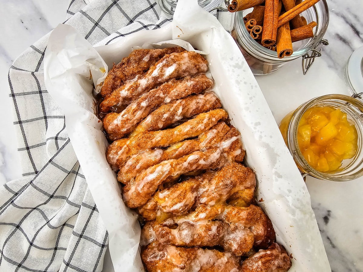 Glazed apple cinnamon biscuit loaf in a parchment lined bread pan