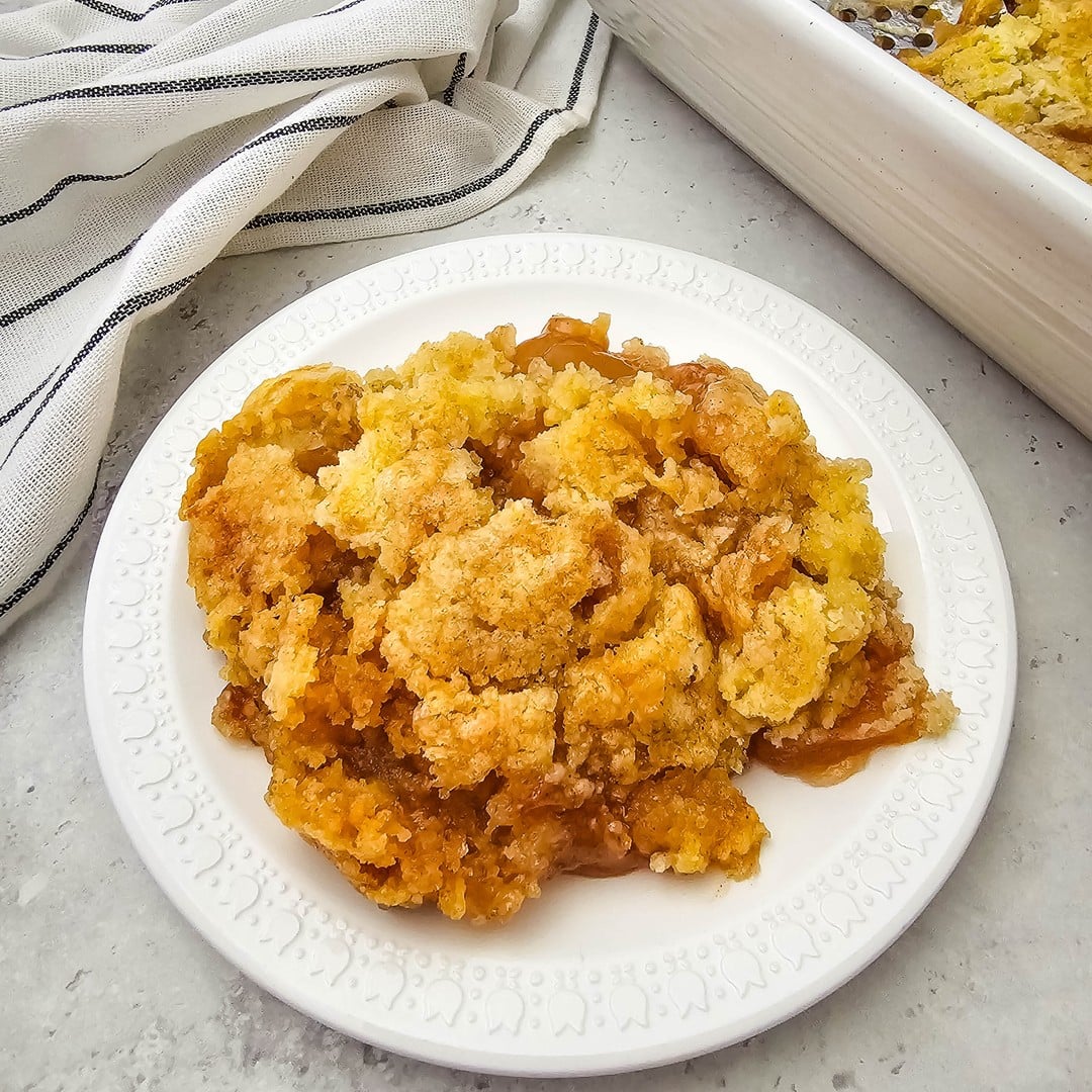 A scoop of apple cobbler showing golden cake topping over apple filling