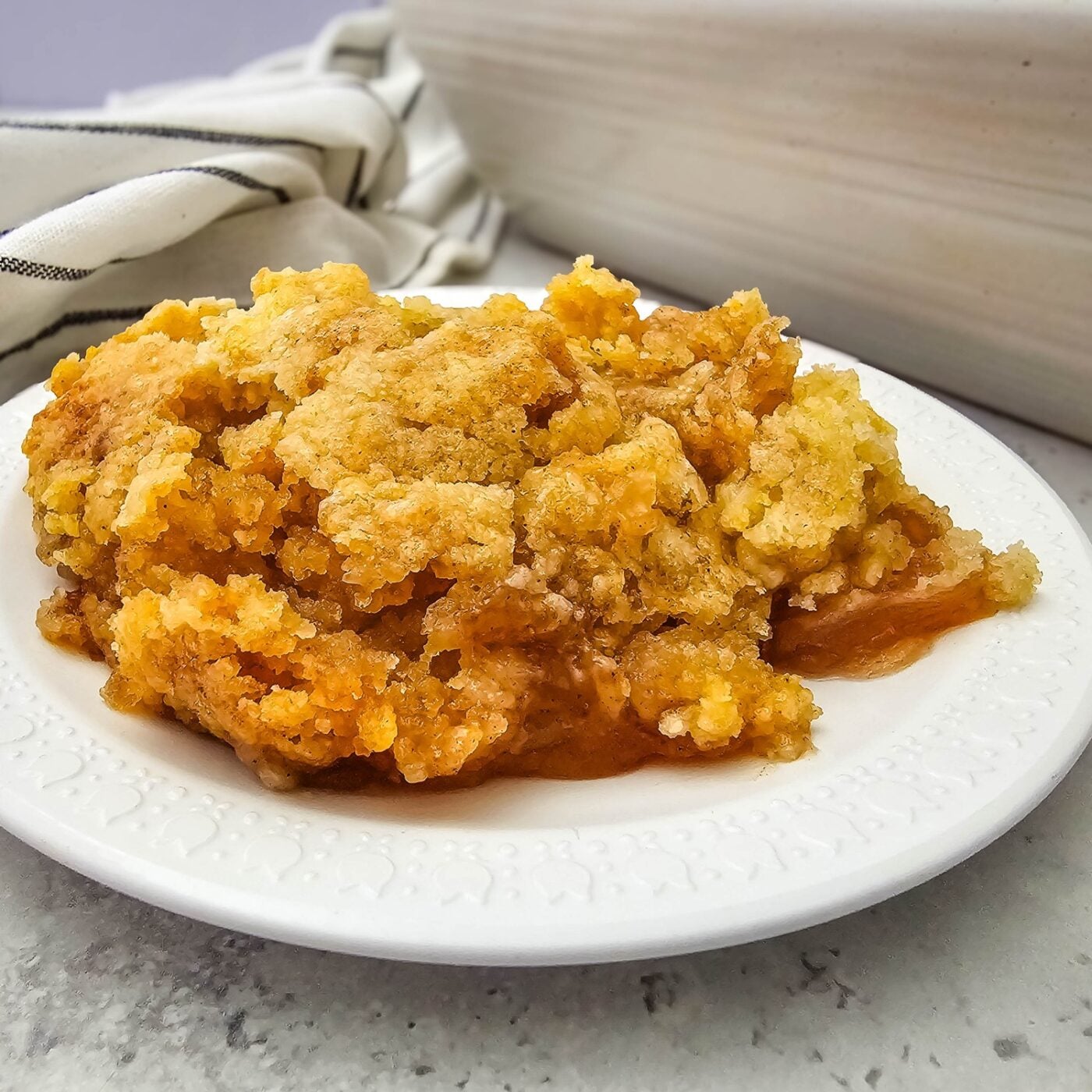 A serving of apple cobbler with apple pie filling and a golden butter-cake crust on a white plate