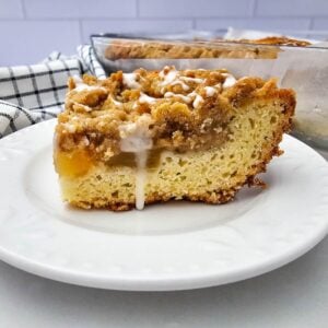 A glazed slice of apple coffee cake showing layers of cake, apple filling and crumb topping