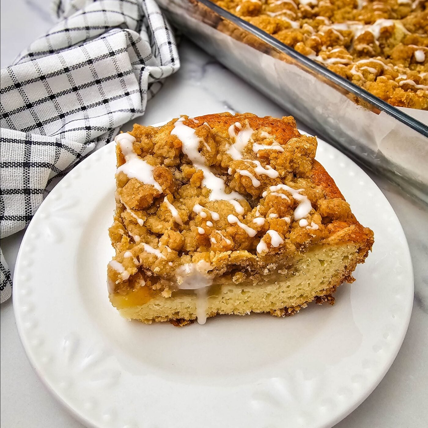 A slice of apple coffee cake with apple pie filling, cinnamon crumble and glaze on a white plate