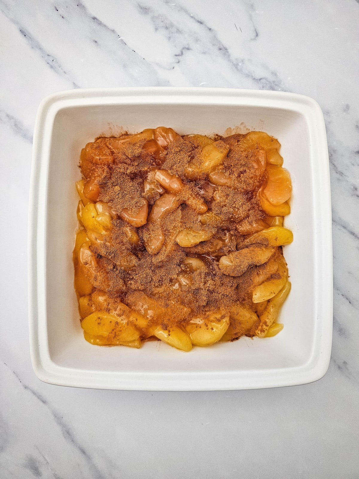 Ground cinnamon sprinkled over apple pie filling