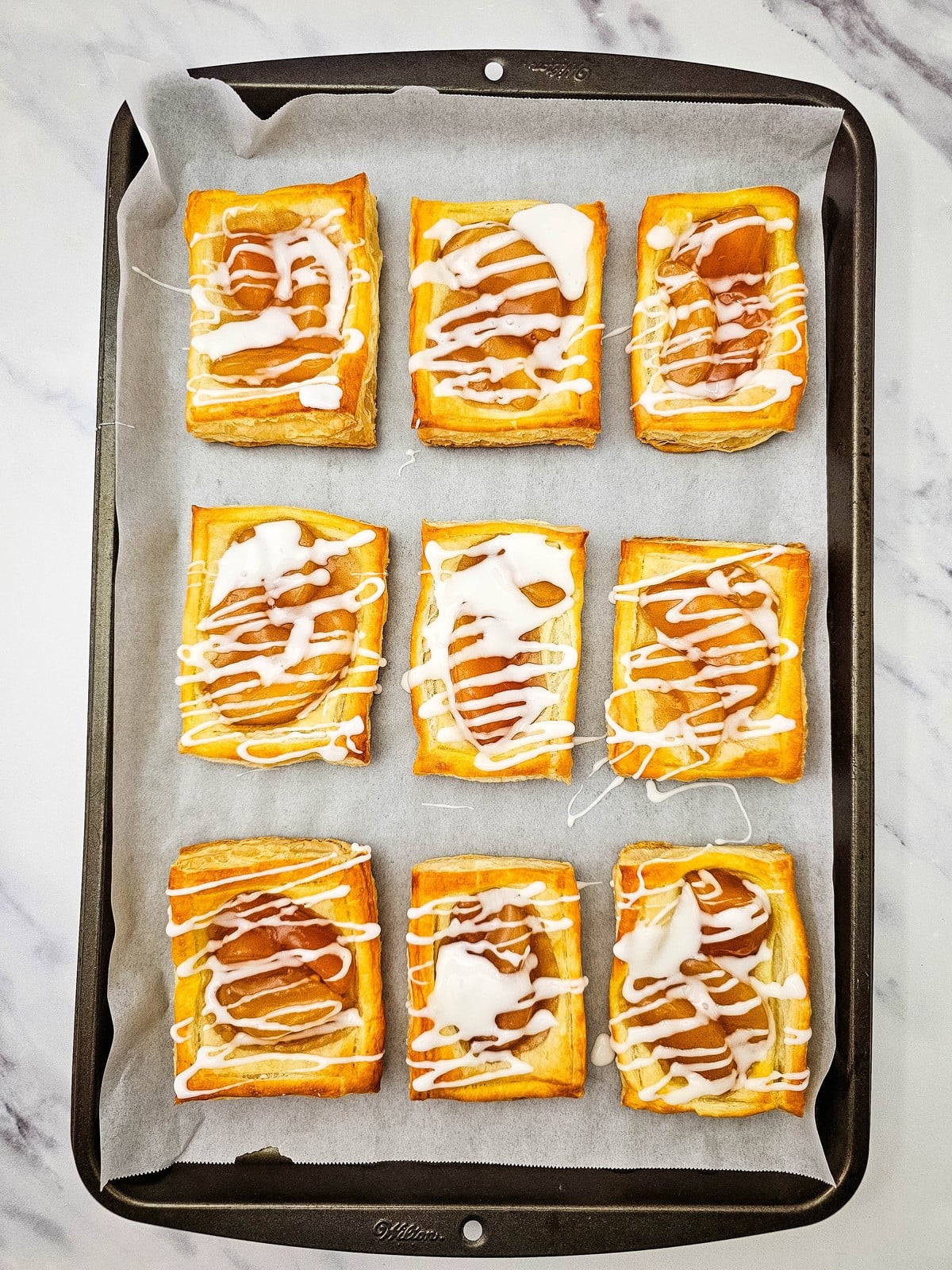 Baked apple danishes drizzled with glaze on a parchment lined sheet pan