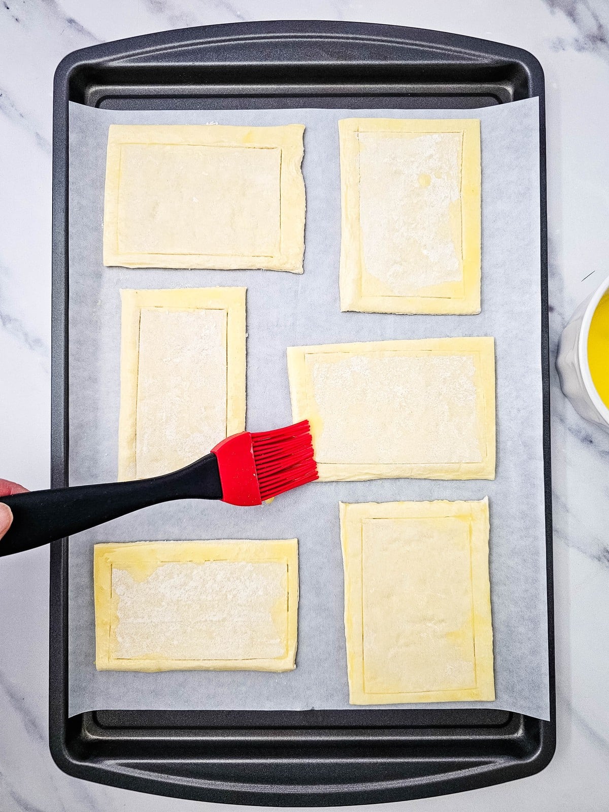 Brushing egg wash on the scored borders of puff pastry rectangles