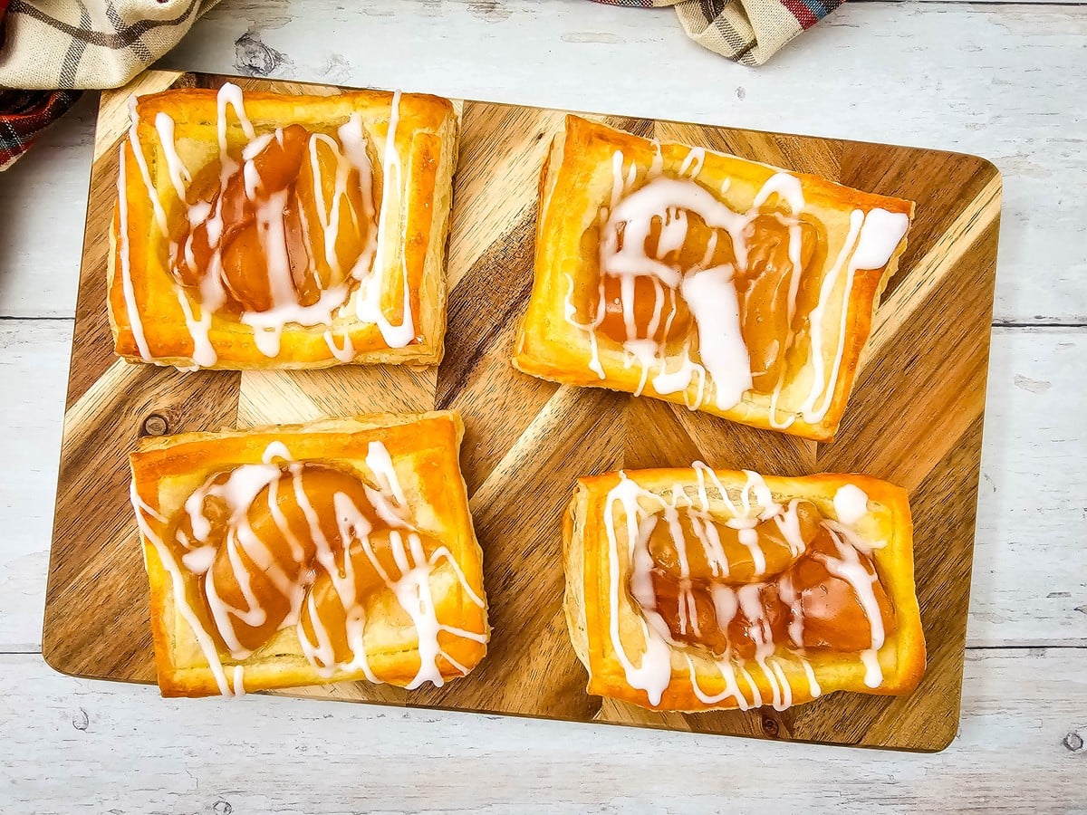 Glazed apple danishes on a wooden board with a plaid towel
