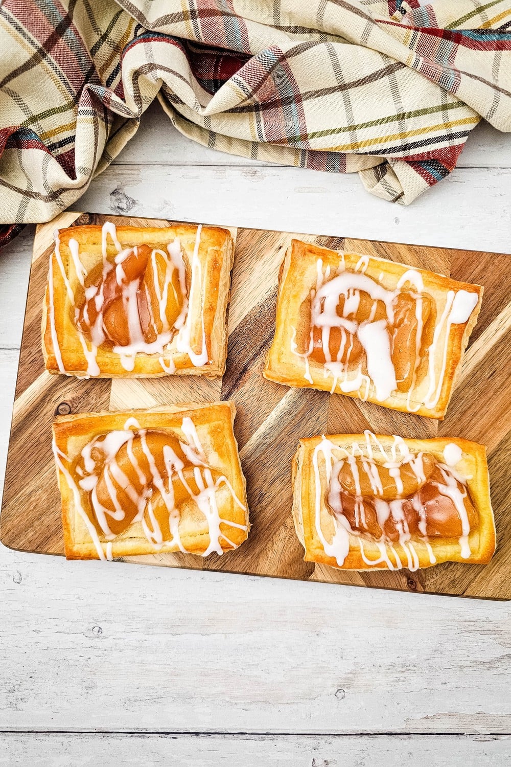 Four glazed apple danishes on a wooden serving board