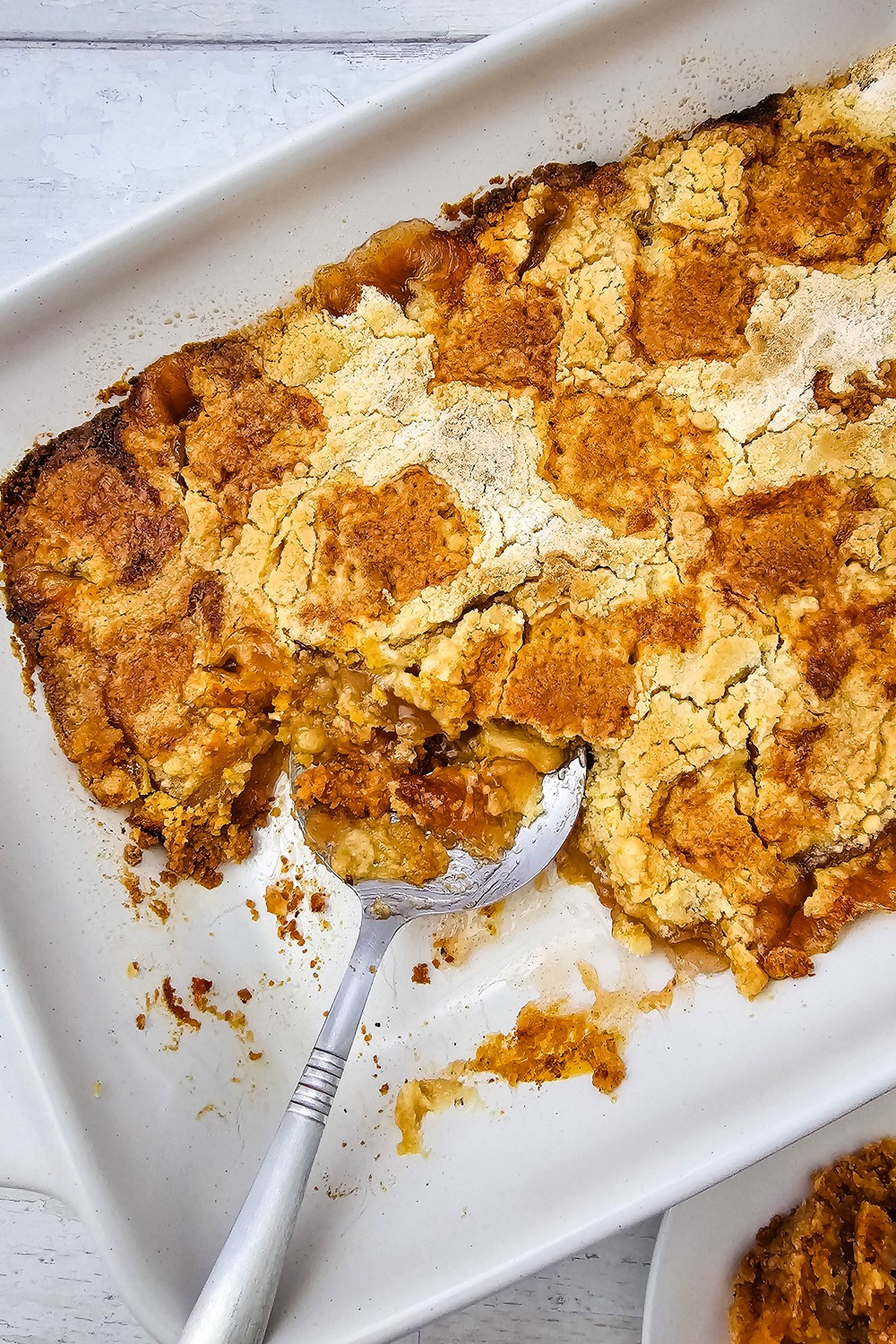 Overhead view of baked apple dump cake in a white dish with a serving spoon