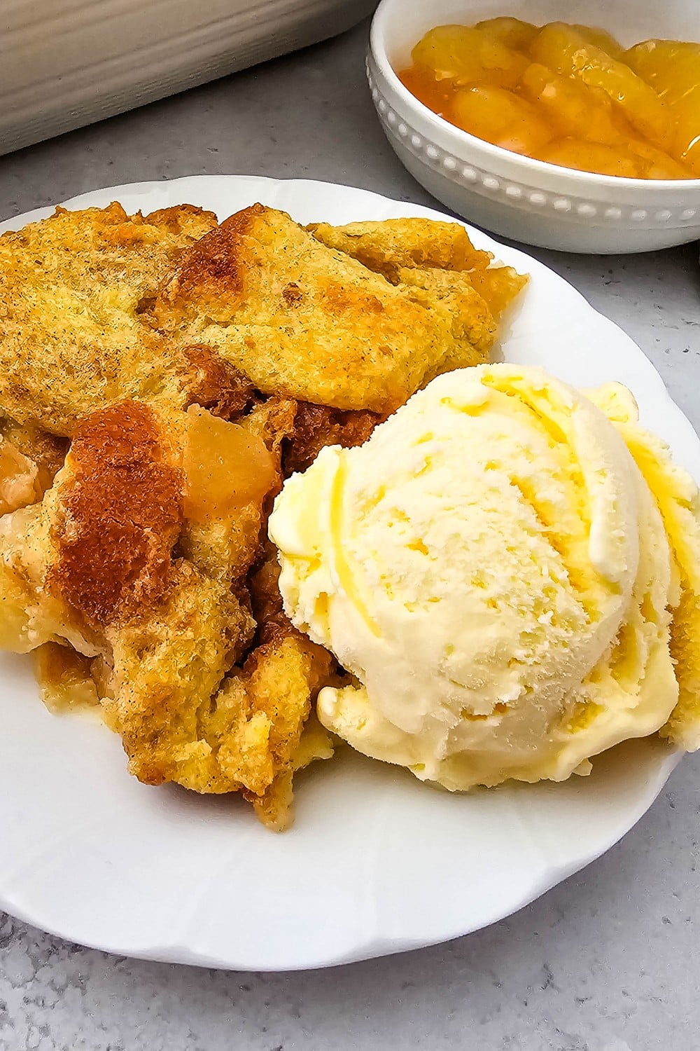 Serving of apple pie bread pudding on a white plate with vanilla ice cream