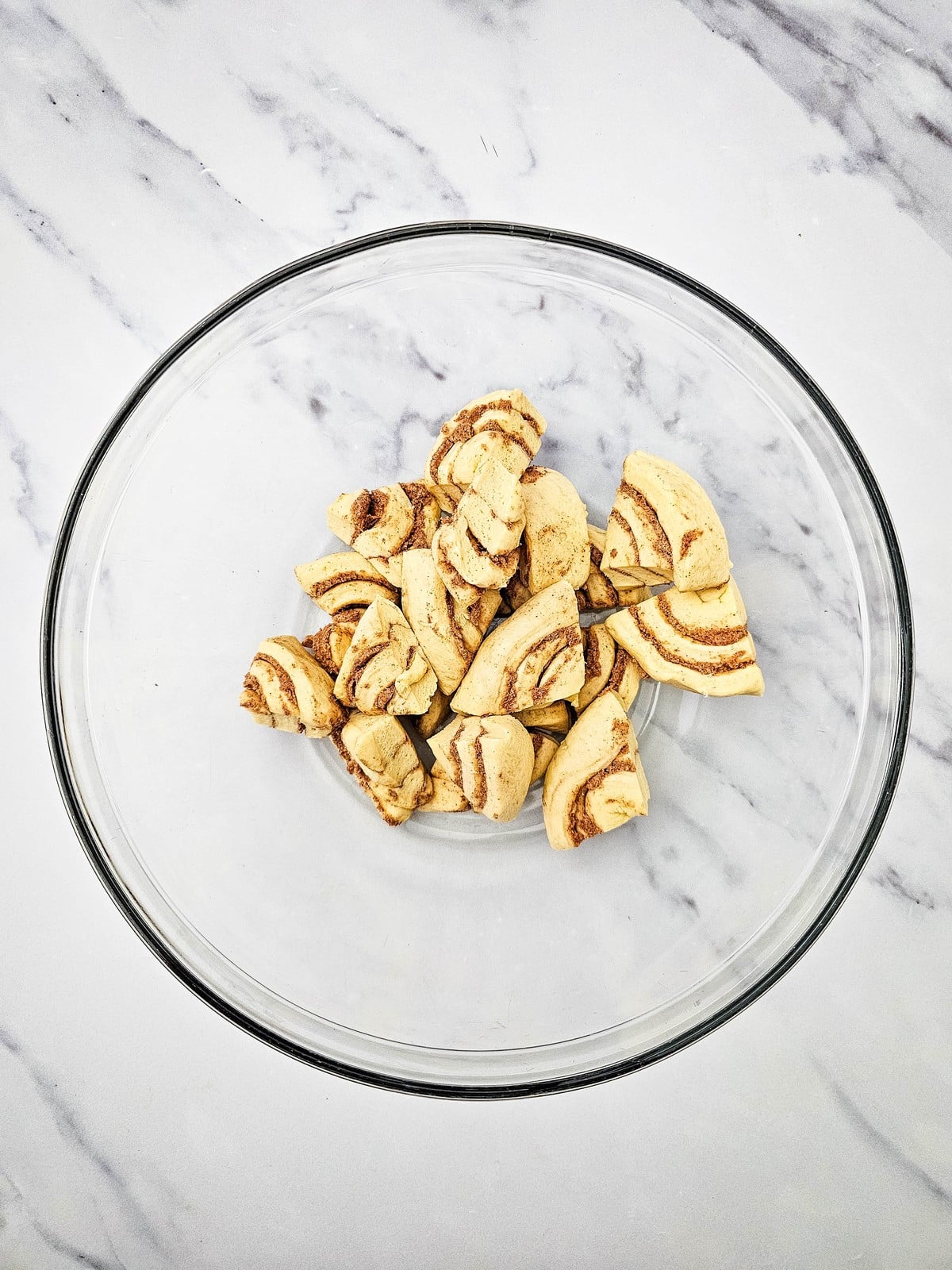 Quartered cinnamon rolls in a glass mixing bowl