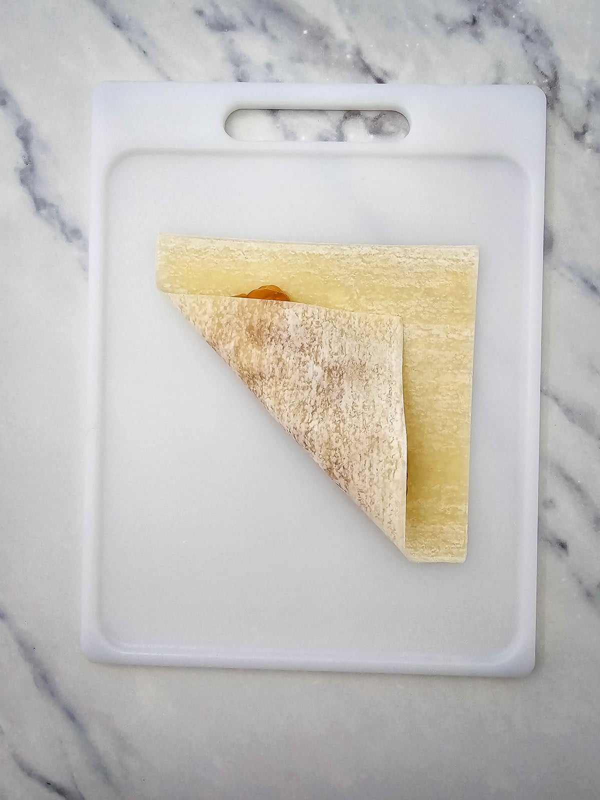 Egg roll wrapper corner folded over the apple filling