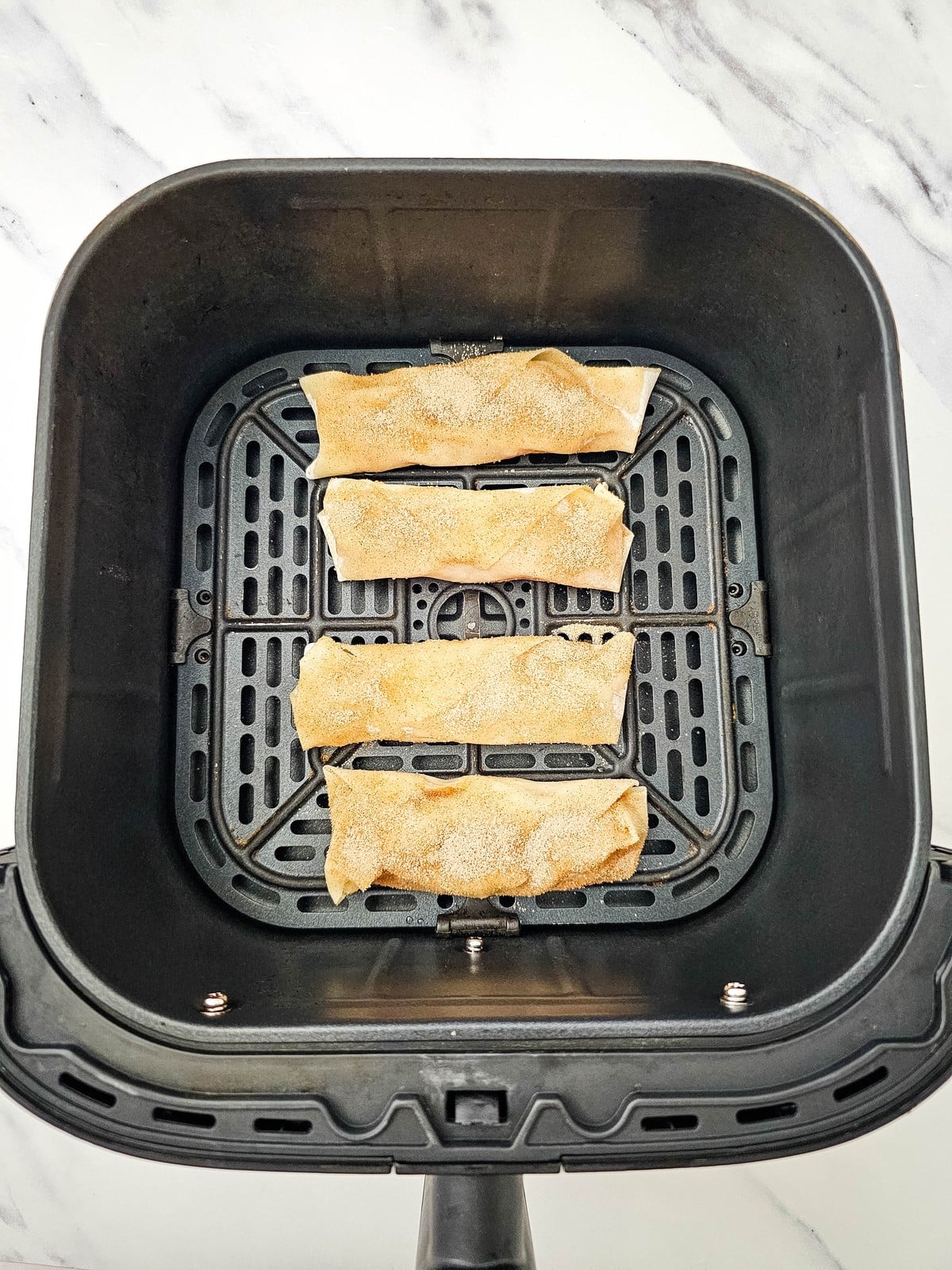 Apple pie egg rolls in the air fryer basket before cooking