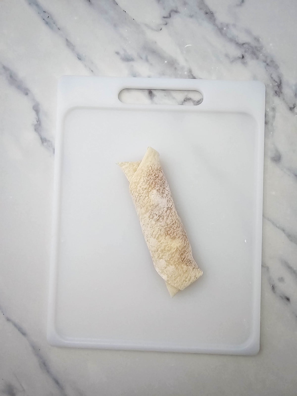 A fully rolled apple pie egg roll on the cutting board