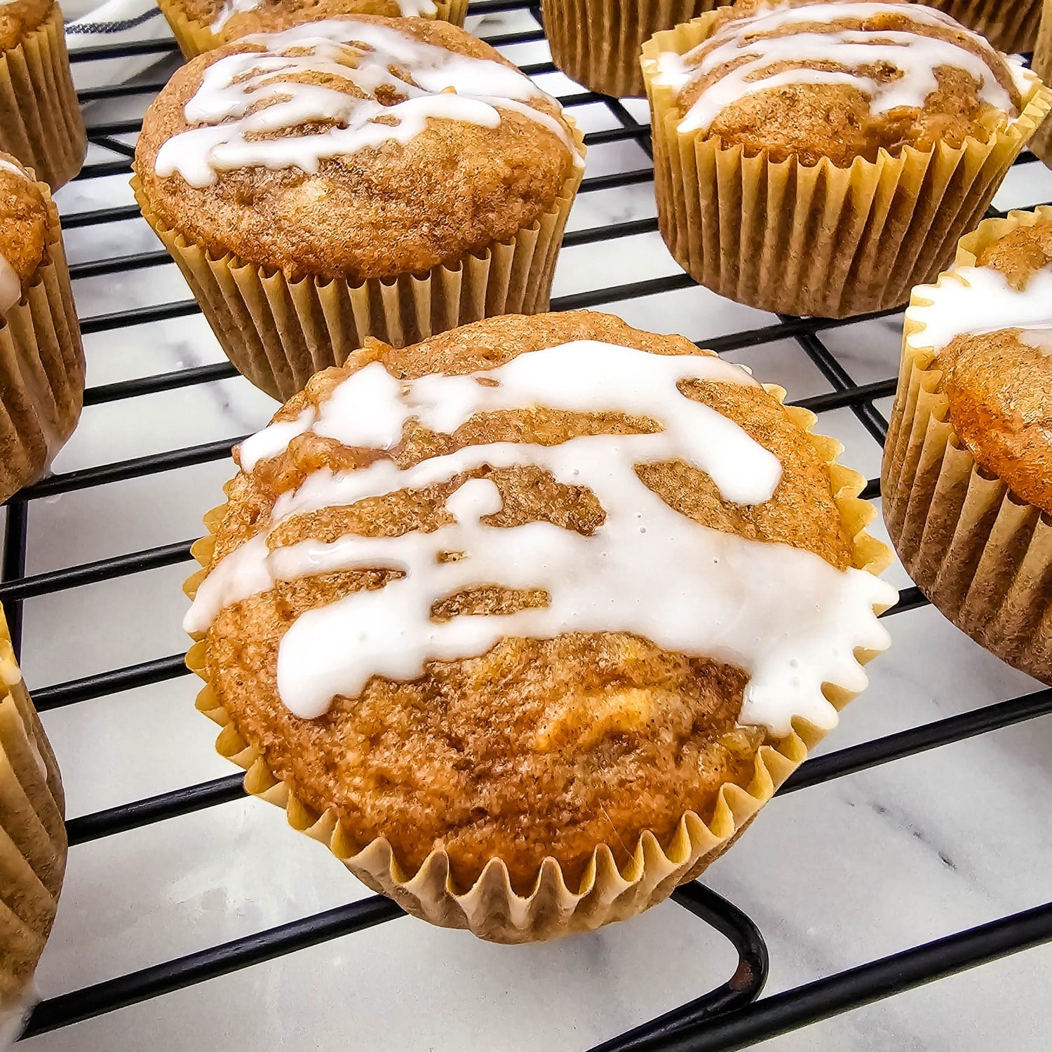 Apple pie filling muffins with a powdered sugar glaze on a cooling rack