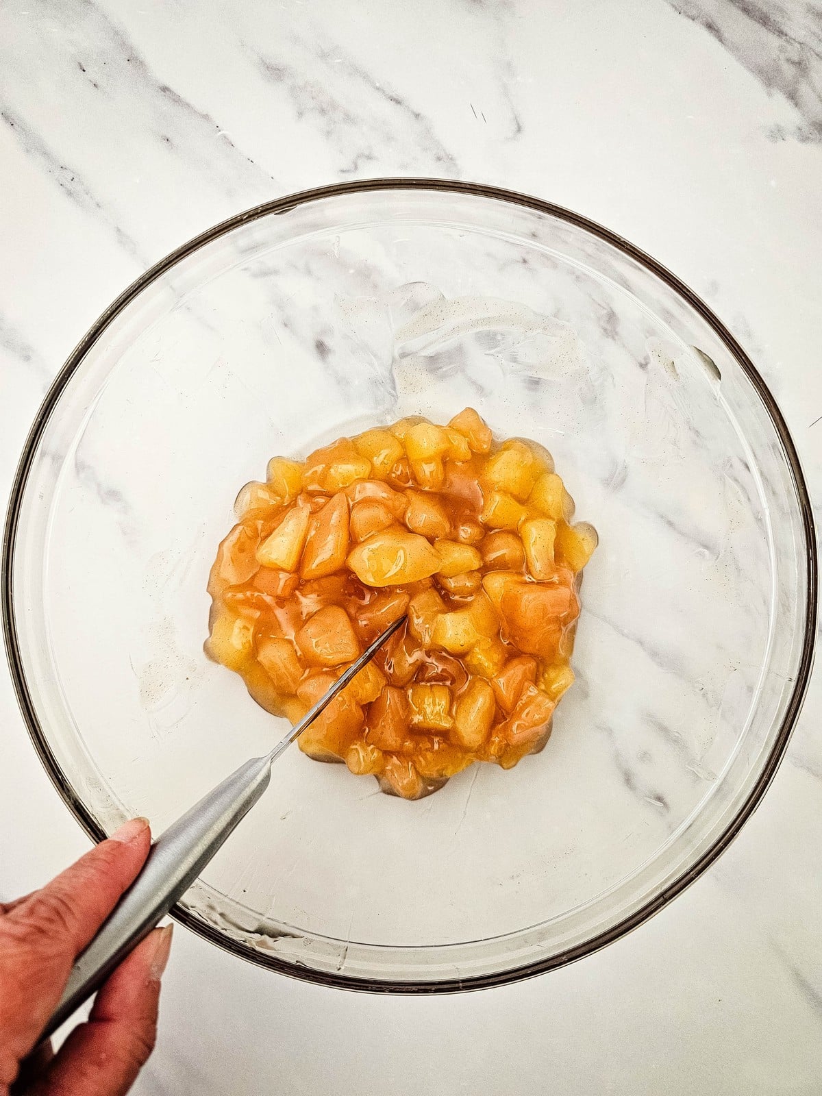 Apple pie filling being cut into small pieces in a glass bowl