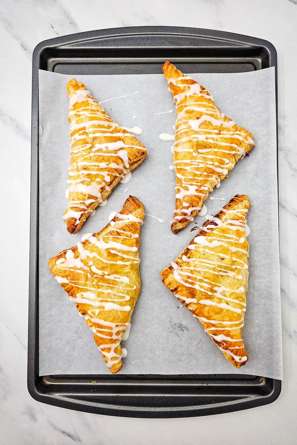 Glazed apple turnovers on a parchment lined baking sheet