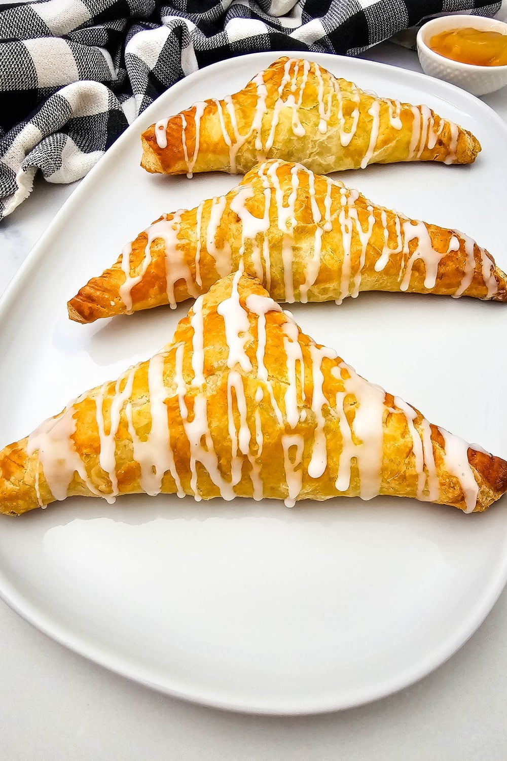 Three glazed apple turnovers on a white platter with apple pie filling for dipping