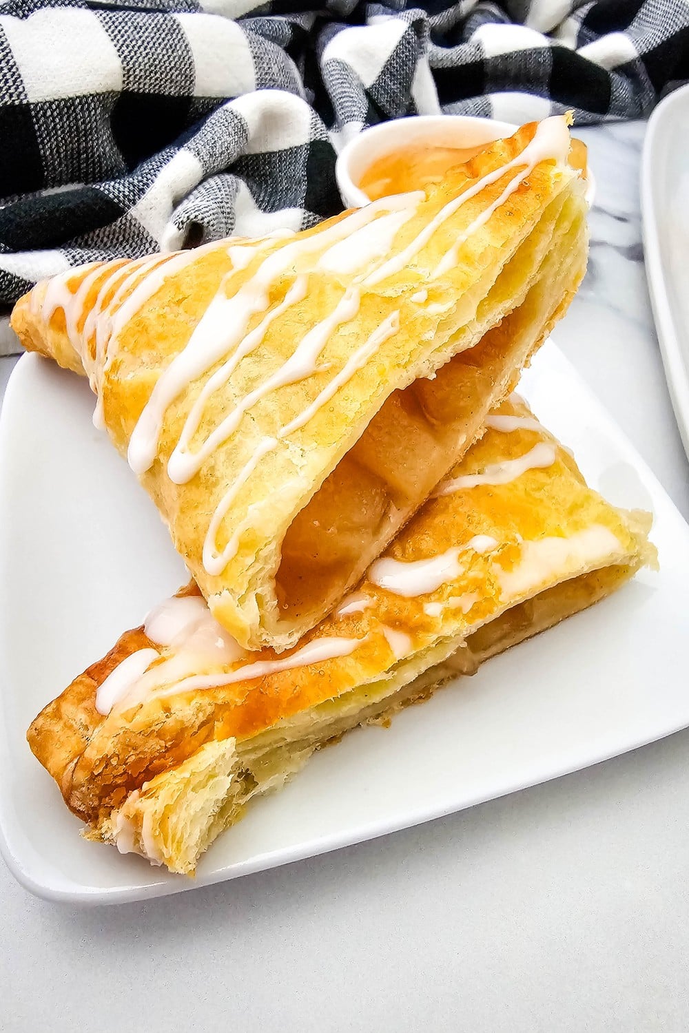 Two glazed apple turnovers stacked on a white plate with apple filling showing