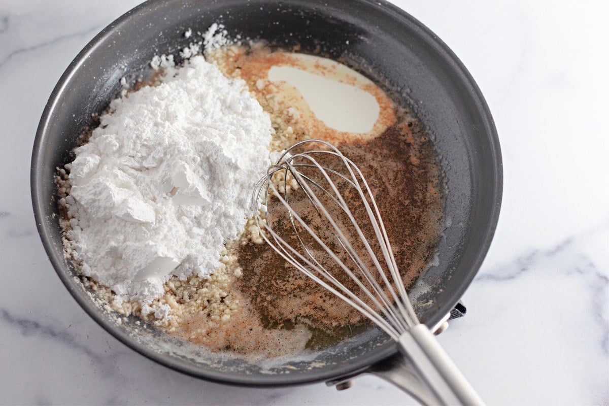 Powdered sugar and vanilla added to browned butter in a skillet with a whisk