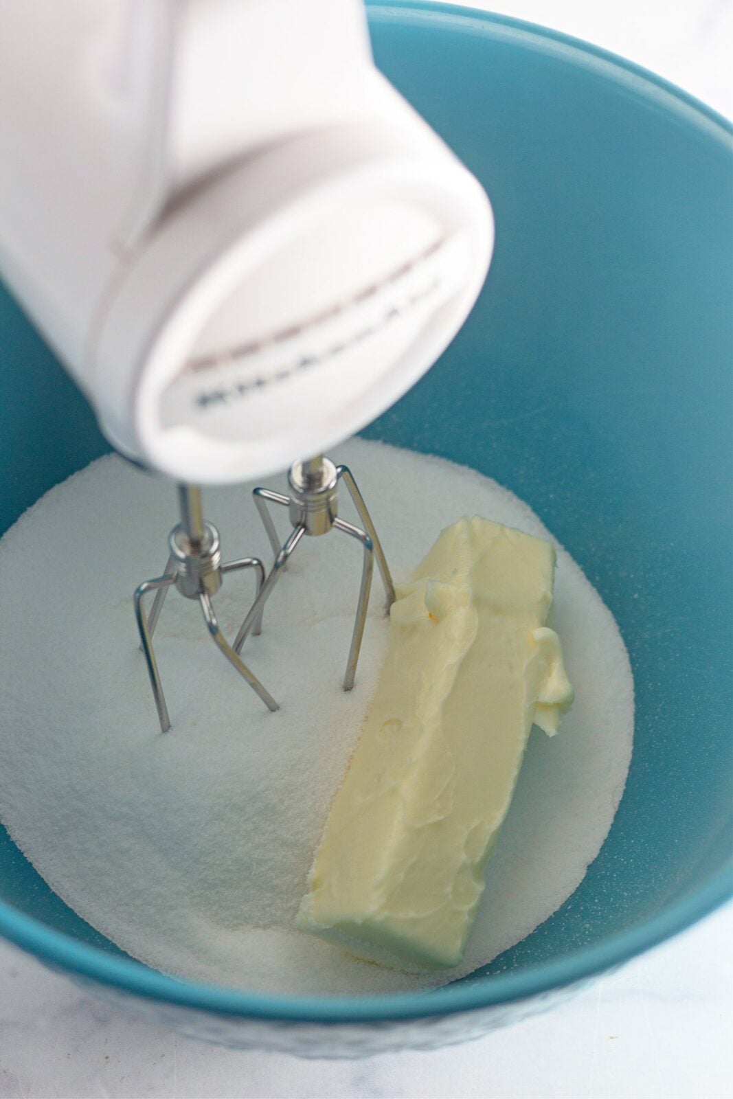 Softened butter and granulated sugar in a blue mixing bowl with a hand mixer