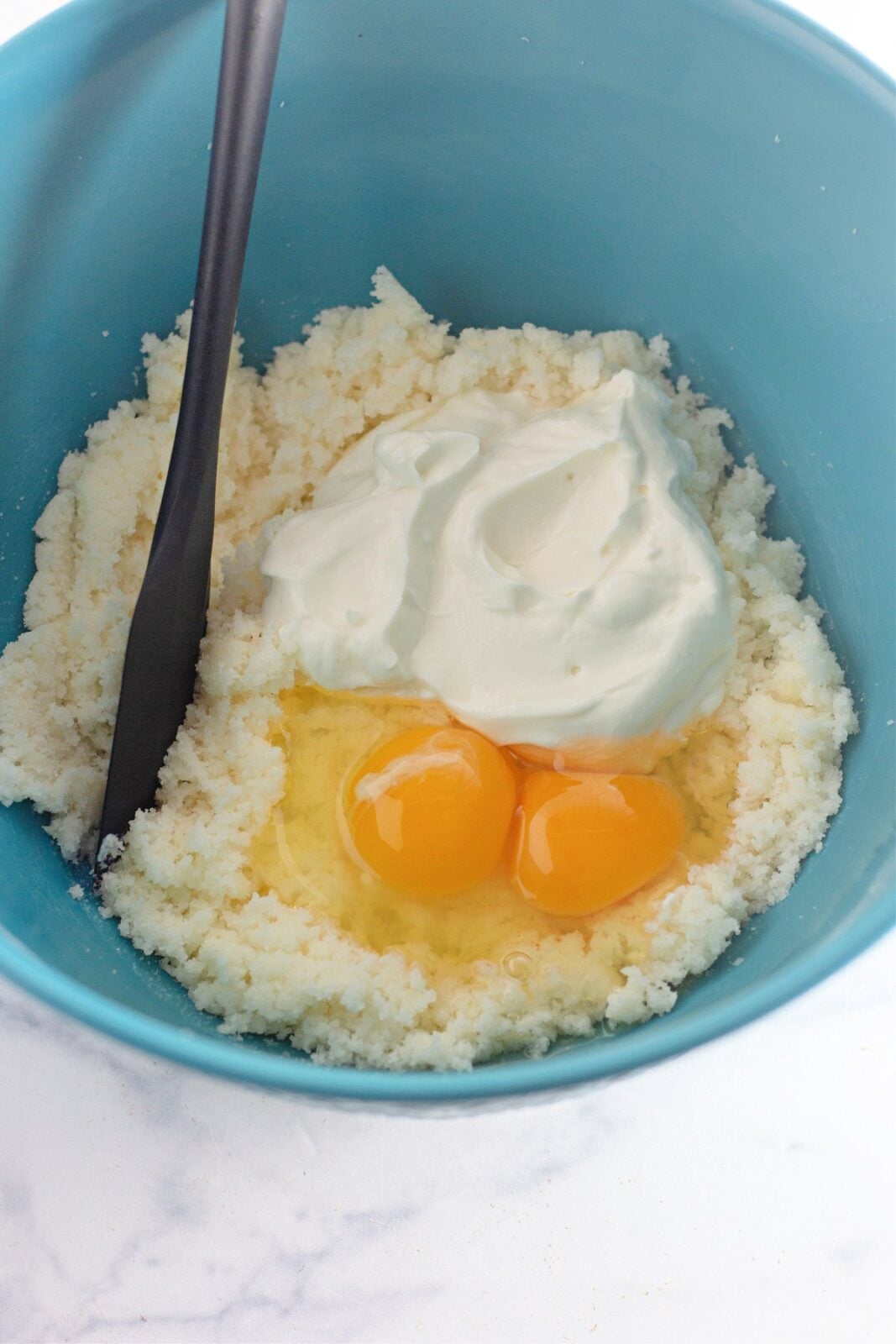 Eggs and sour cream added to creamed butter and sugar in a blue bowl