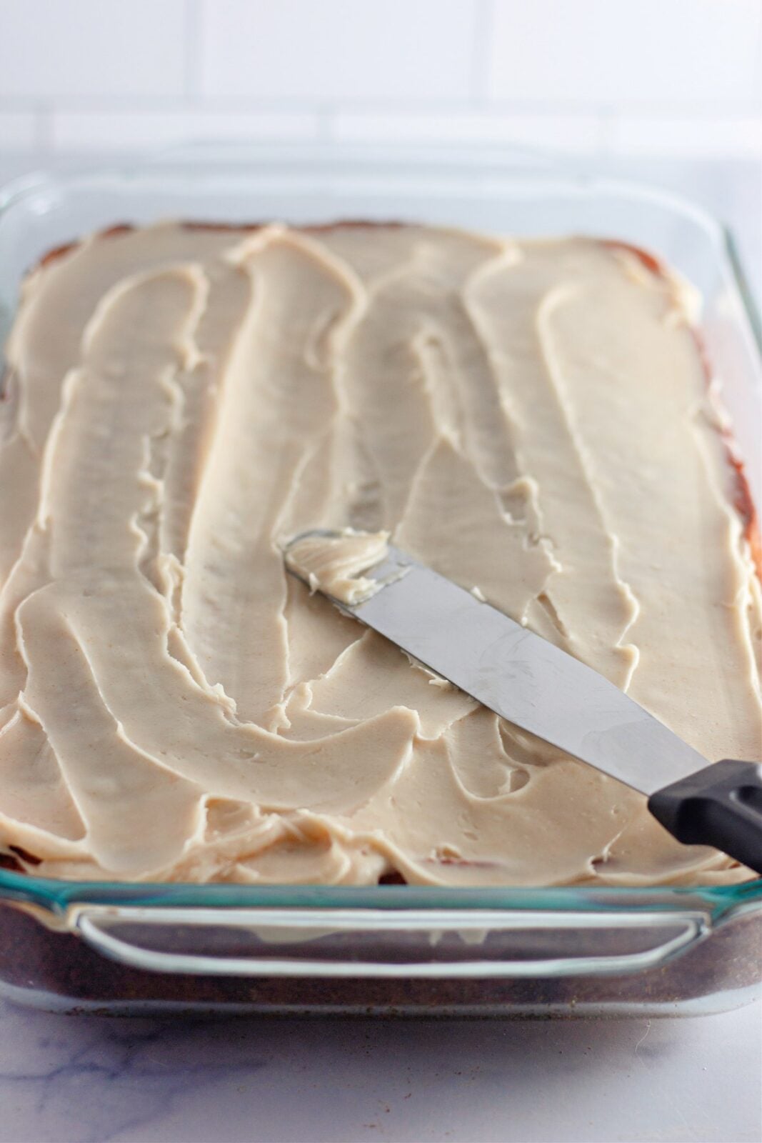 Frosted banana coffee cake with an offset spatula smoothing the browned butter frosting
