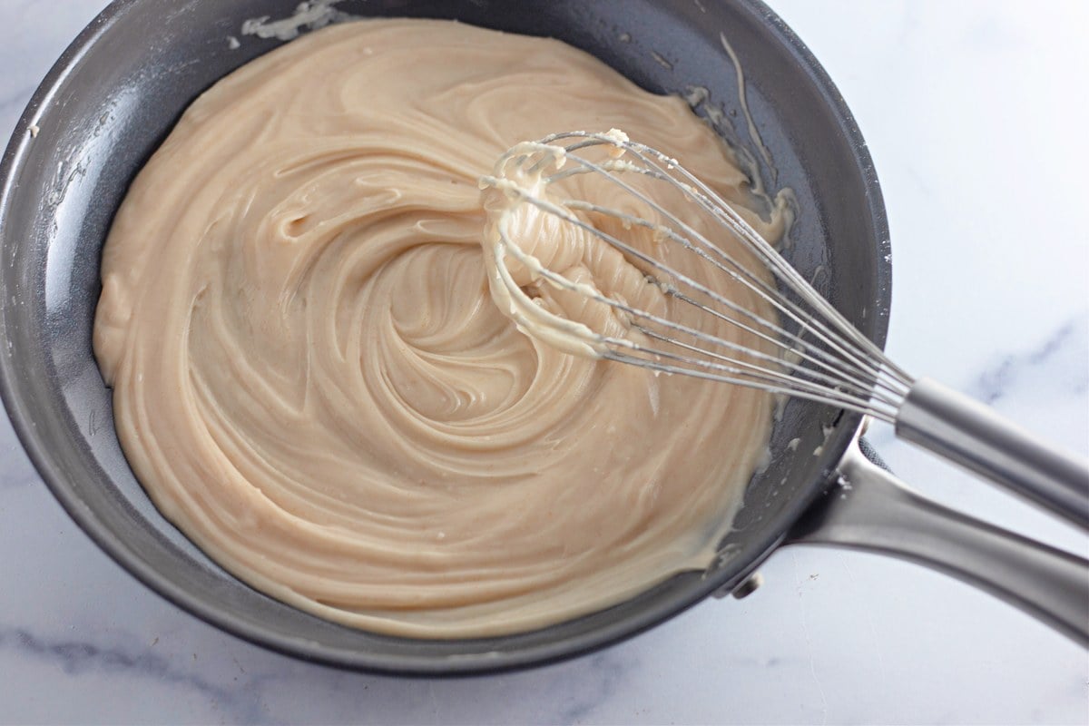 Smooth glossy browned butter frosting whisked with heavy cream in a skillet