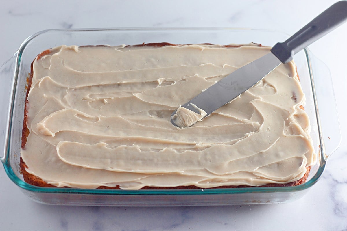 Spreading browned butter frosting over the cooled banana coffee cake with an offset spatula