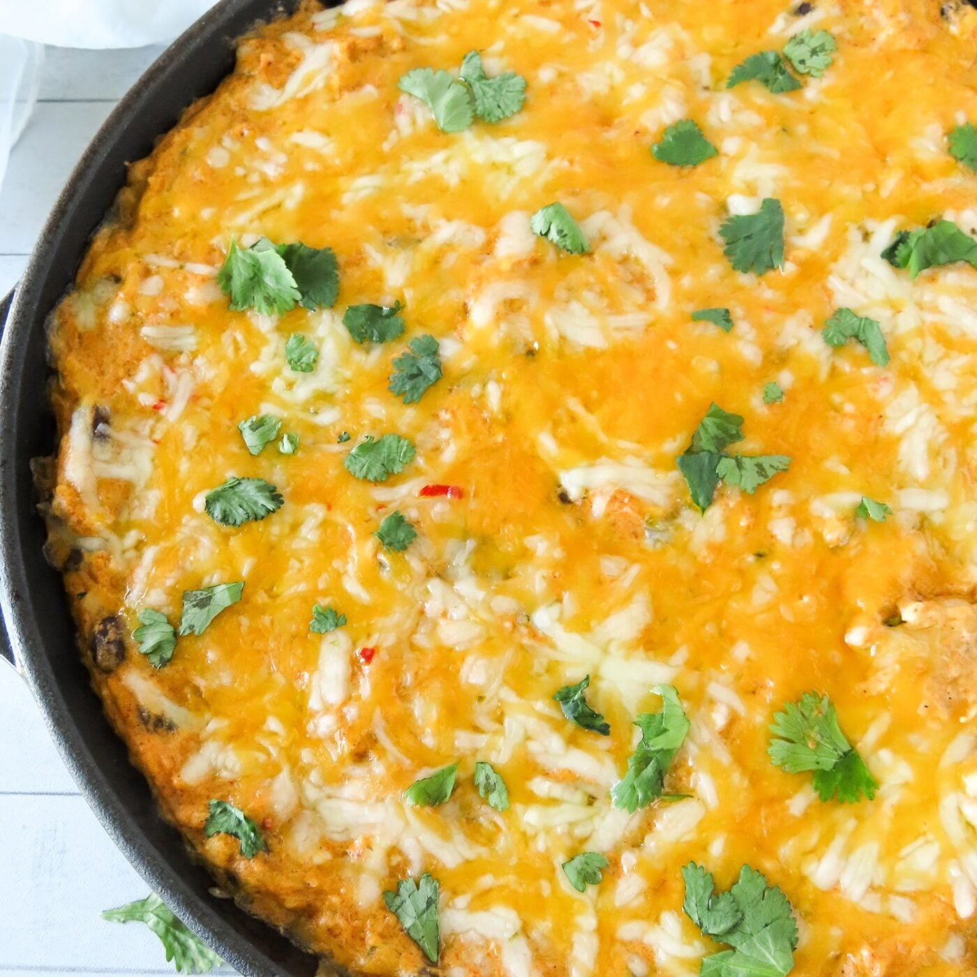 Baked chicken enchilada dip with melted cheese and cilantro in a cast iron skillet, close up