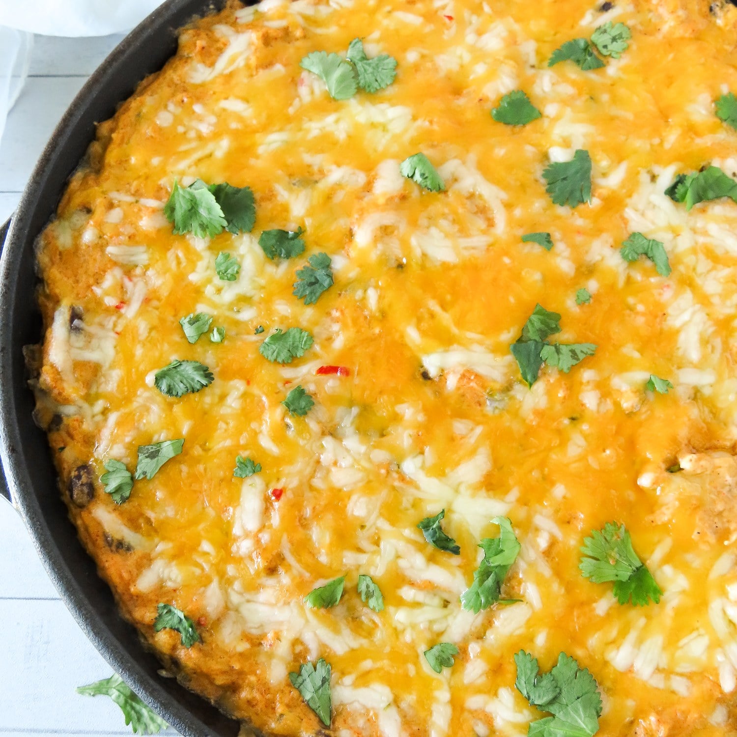 Baked chicken enchilada dip with melted cheese and cilantro in a cast iron skillet, close up