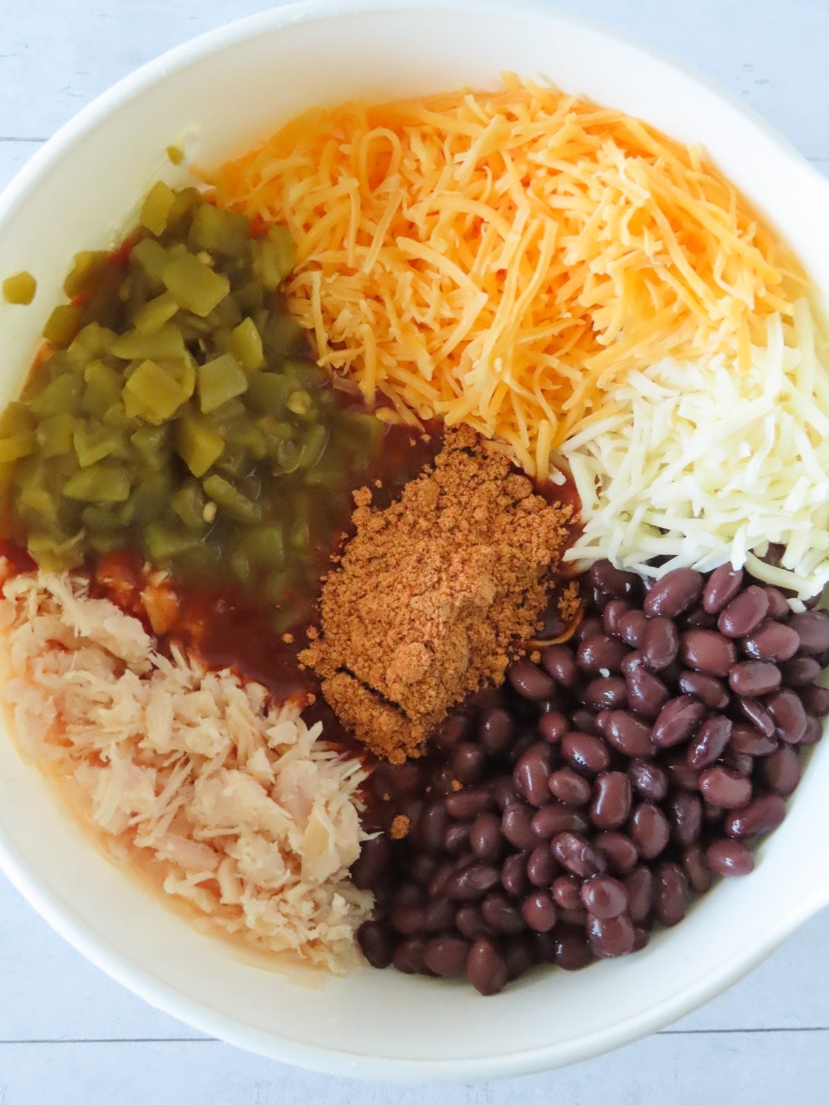 Shredded chicken, cheeses, black beans, green chiles, taco seasoning, and enchilada sauce in a mixing bowl
