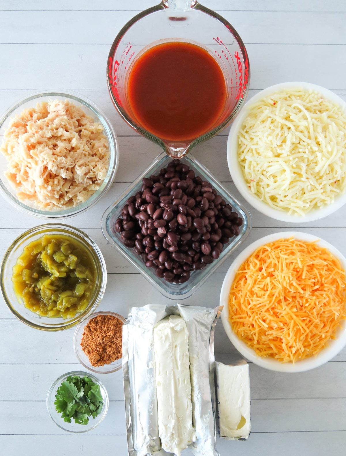 Chicken enchilada dip ingredients: shredded chicken, cream cheese, black beans, cheeses, green chiles, enchilada sauce, and taco seasoning