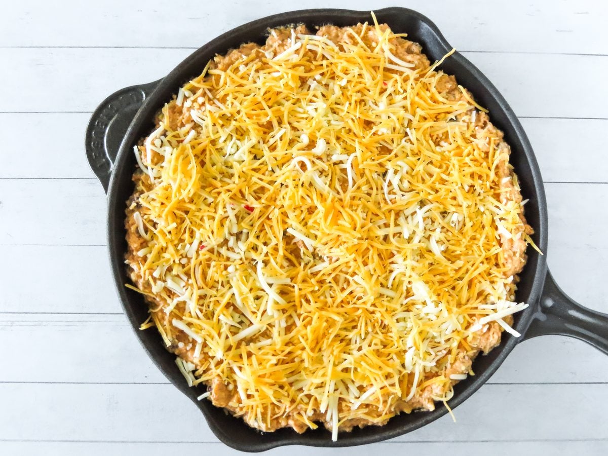 Skillet dip topped with shredded cheddar and pepper jack before baking